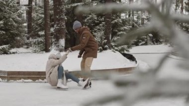 Genç Afrikalı adamın neşeli kıvırcık saçlı melez kadının parkta buz pateni yaparken ayakta durmasına yardım ettiği geniş bir çekim.