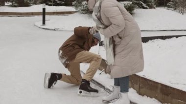 Genç melez bir kadının parktaki buz pateni sırasında güler yüzlü Afro-Amerikan genç adamın ayağa kalkmasına yardım ettiği geniş bir çekim.
