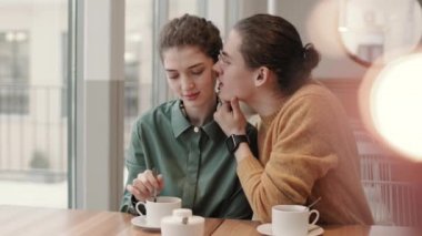 Kafe masasında oturan ve yakınlarda oturan çekici genç bayanı öpen yakışıklı bir adamın orta boy fotoğrafı.