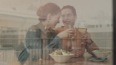 Kafkasyalı güzel bir kadın ve genç erkek arkadaşının restoranda yemek yerken kadeh tokuşturduğu orta boy bir fotoğraf.