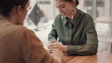 Kafe 'de oturan ve önünde kahve içerken kıvırcık saçlı genç bir adamla konuşan, zarif giysiler giyen beyaz bir kadın.