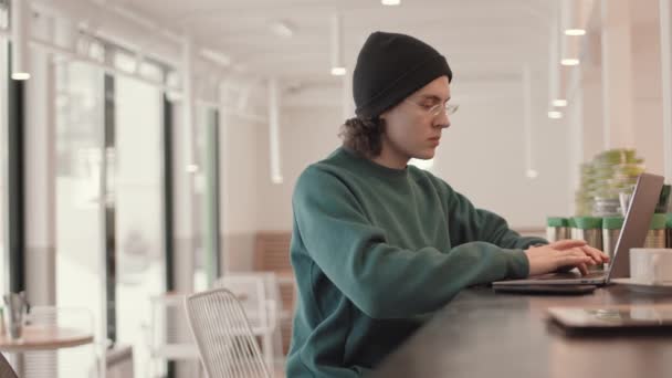 穿着便服和眼镜坐在咖啡店里 在笔记本电脑键盘上输入程序代码的年轻嬉皮士男子中的一张照片 — 图库视频影像