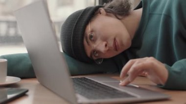 Sokakta takılan ve gözlük takan genç ve yorgun adamın dizüstü bilgisayarın önünde oturması, çalışmaya çalışması ve sonra uykuya dalması.