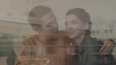 Orta halli mutlu beyaz bir adam ve çekici genç karısı restoran masasında oturmuş birbirlerine sarılıyorlar.