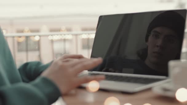 年轻的男性程序员头戴便服 帽子和眼镜 坐在咖啡桌旁 在笔记本电脑上工作 从肩膀上看过去 — 图库视频影像