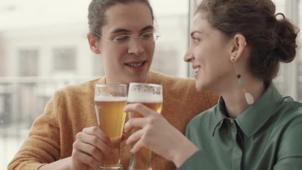 若い白人男性と魅力的な女性がレストランでスタイリッシュな服を着て ビールグラスをクリックしてビールを飲みます — ストック動画