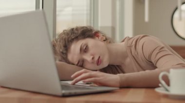 Yorgun, kıvırcık saçlı, beyaz iş kadınının laptopun masasında oturması ve iş sırasında uykuya dalması.
