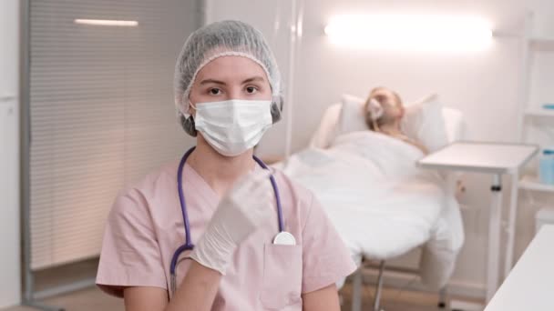 胸像を身に着けている患者の病棟で若い白人女性医師のチェストアップPov 使い捨ての帽子 首周りの聴診器 マスクを脱いで カメラを見て 長日後の医療従事者の肖像 — ストック動画