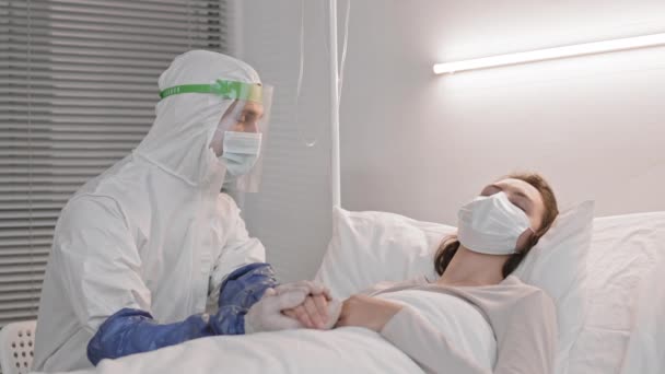 穿着全套防护服的中工 头戴口罩 坐在病床附近 睡在病房里 医生照顾女人 检查体温 — 图库视频影像
