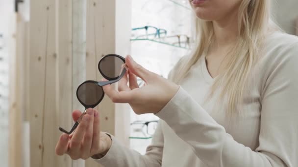 Średnie Ujęcie Nierozpoznawalnej Blondynki Stojącej Sklepie Optycznym Okularami Przeciwsłonecznymi Rękach — Wideo stockowe