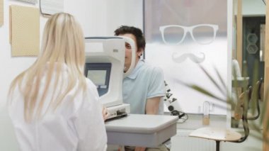 Sarışın kadın göz doktorunun, tonometreye bakan koyu renk saçlı beyaz adamın görüşünü kontrol edişinin arka görüntüsü.