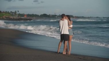 Genç, zayıf, beyaz, romantik çiftin dans etmesi kumlu okyanus kıyısında kucaklaşması, dalgaların kıyıya vurması, güzel sıcak bir günde köpeklerinin etraflarında koşması.