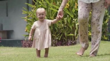 Orta boylu, sarı saçlı, sevimli elbiseli beyaz bir kız çocuğu. Kameraya gülümsüyor, bahçede yeşil çimlerde yürüyor, tanınmayan bir annenin elini tutuyor.