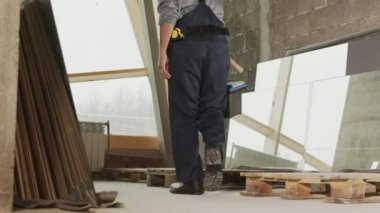 Tracking right of Mixed-Race female construction specialist walking, carrying toolbox, sitting down on wooden pallet, taking off helmet, and wiping off sweat of forehead after hard work