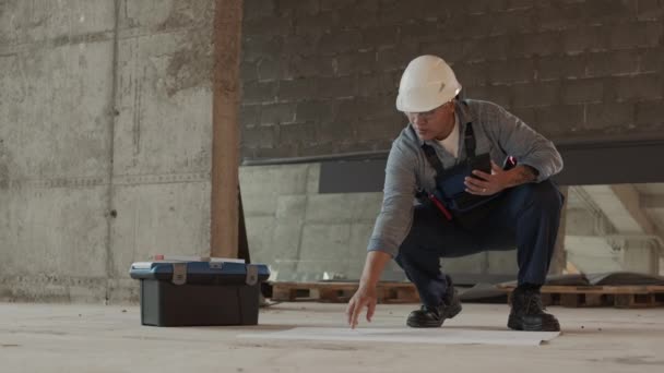 Long Shot Concerned Construction Specialist Wearing Protective Goggles Helmet Squatting — Vídeo de Stock