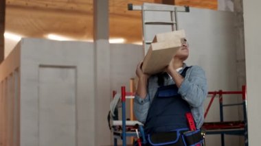 Side view medium shot of Mixed-Race female construction worker wearing helmet and goggles, holding pile of wooden beams, looking and turning around