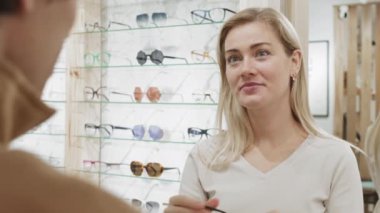 Tanımlanamayan erkek optometristin, gözlükçüden yeni gözlük seçen sarı saçlı kadına yardım edişi.