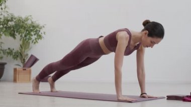 Spor kıyafetleri giyen beyaz bir kadının yoga egzersizleri yaptığı geniş açılı bir çekim.