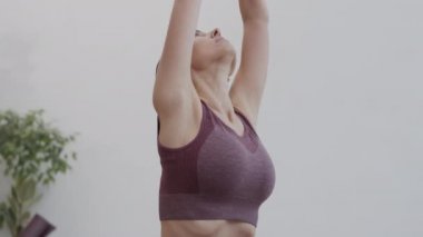 Spor kıyafetleri giymiş güzel beyaz bir kadının yoga minderinin üzerinde oturması ve nefes alma egzersizleri yapması.