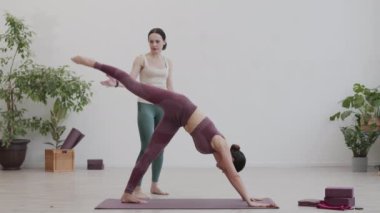 Kadın koçun spor salonundaki kauçuk paspas üzerinde esneme egzersizleri yapmasına yardım ettiği geniş açı.