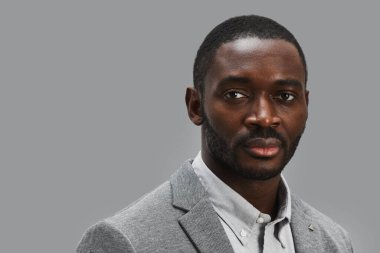 Özgüvenli Afro-Amerikan işadamının gri arka planda dururken kameraya bakan portresi