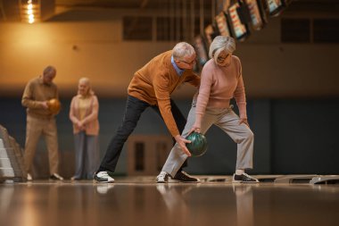 Bowling salonunda aktif eğlenirken modern yaşlı çiftin geniş açılı yan görüntüsü, fotokopi alanı.