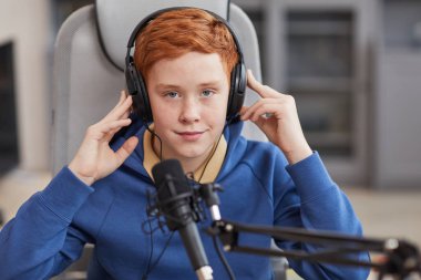 Podcast ya da online yayın yaparken mikrofona konuşan ve kulaklık takan kızıl saçlı gencin portresi.