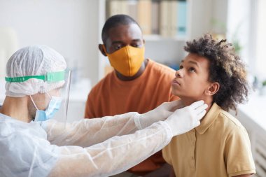 Erkek doktor portresi Afro-Amerikan çocuğu muayene ediyor ve muayene sırasında boğaz elle muayene ediyor.