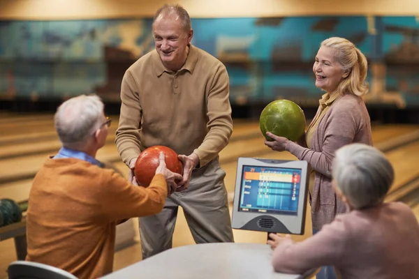 Group of senior people playing bowling together while enjoying active entertainment at bowling alley, copy space