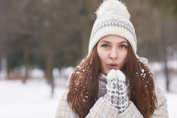 Ön manzara, kışın örgü şapka ve eldiven takan mutlu genç bir kadının portresi. Karla kaplı kameraya bakarken, kopyalama alanı.