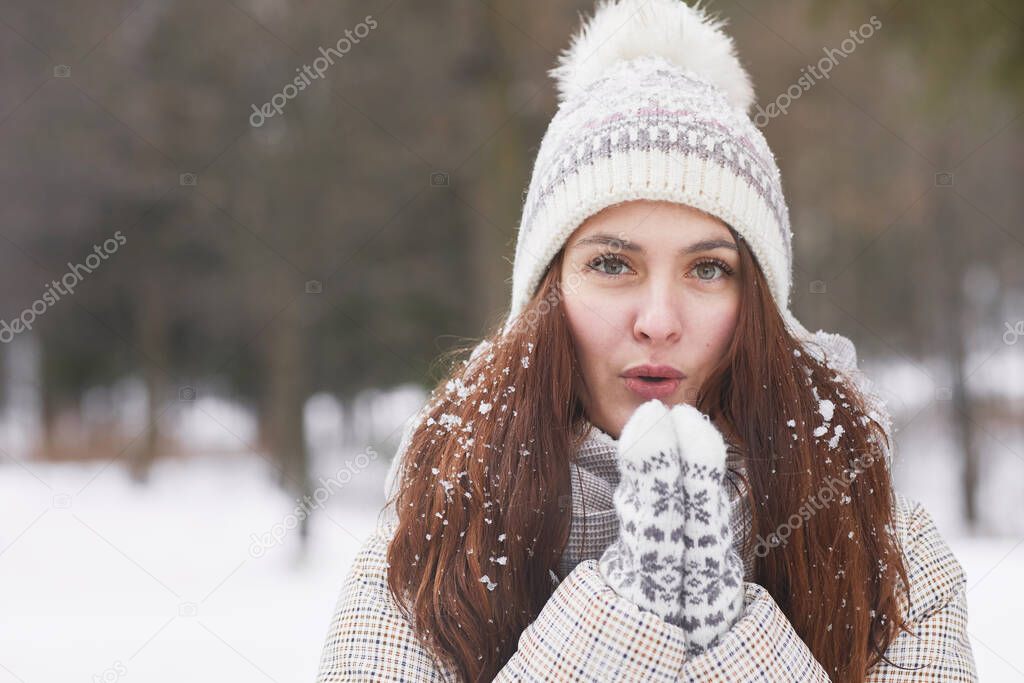Front view close up portrait of happy young woman in winter wearing knit hat and mittens while looking at camera covered in snow, copy space