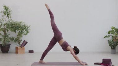 Geniş açıda beyaz kadın spor giyimli kadın lastik paspas üzerinde pilates yaparken görülüyor.