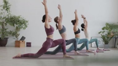 Yoga stüdyosunda yoga yapan dört beyaz kadın yoganın geniş açılı görüntüsü.