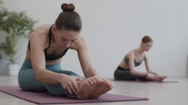 Spor salonundaki lastik paspasın üzerinde oturan ve esneme egzersizleri yapan genç ve güzel görünümlü bir sporcuyu kilit altına almak.