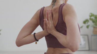 Arka tarafta, spor kıyafetleri giymiş, elleri arkada poz veren, tanınmayan kadın yogayı görüyoruz.