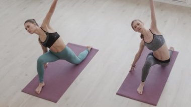 Spor kıyafetleri giymiş iki genç Yogi 'nin kapalı yoga dersleri sırasında esneme egzersizleri yaparken yüksek açılı görüntüsü.
