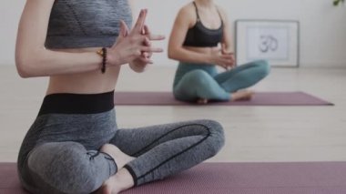 Tanımlanamayan iki kadının şık spor giysiler giyip yoga eğitimi sırasında yoga minderlerinde poz vermelerini ve meditasyon yapmalarını.