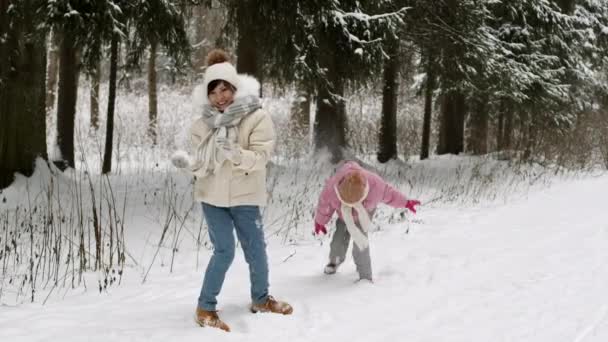 幸せなアジアの母親と子供の長いショットは 雪の冬の森の中で雪玉を遊んで 楽しさを持って ザボンやスカーフ笑って帽子 パフジャケットを身に着けている — ストック動画
