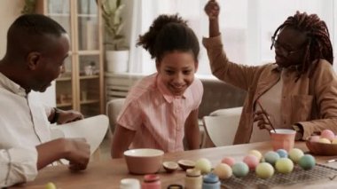 Orta ölçekli Afrikalı kadın ve erkek yemek odasında oturmuş, konuşuyorlar, 10 yaşındaki kızları katılıyor, ebeveynler sarılıyor ve çocukları öpüyor.