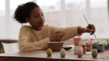 Masanın üzerinde duran çeşitli renklerde yumurta şekilli küçük figürlerin sağ izini sürerken arka planda bulanık kişi daha fazla resim çiziyor.