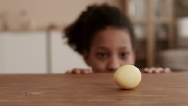 黄色の卵が木製の表面に回転し テーブルでそれを見てぼやけた人は それを取って消えます — ストック動画
