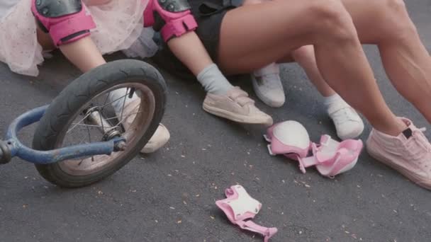 一名无法辨认的年轻女子和她的两个穿着运动鞋的孩子在溜冰后坐在柏油路上 她的双腿中弹 — 图库视频影像