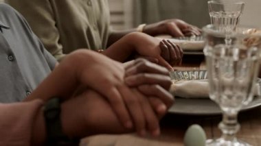 Üç tanınmayan insanın el ele tutuşup akşam yemeğinden önce dua edişinin yan görüntüsü.