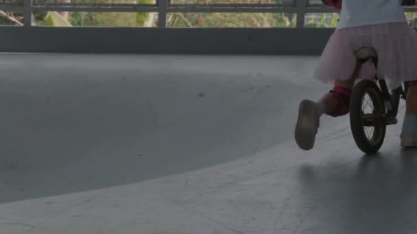 在室内溜冰场 白人少女穿着休闲装 戴着五颜六色的安全帽 手肘和膝盖垫骑自行车的全景 — 图库视频影像