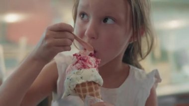 Uzun kahverengi saçlı, kolsuz tişörtlü, kafede vitrinin önünde duran ve lezzetli dondurmalar yiyen beyaz kız.