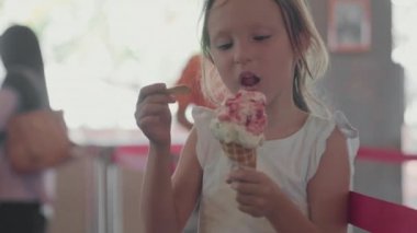 Kafede uzun kahverengi saçlı, orta boy beyaz bir kız dondurmasının tadını çıkarıyor.