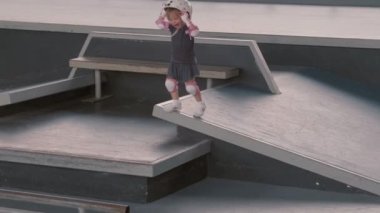 Sarışın, beyaz bir kızın etek, tişört, güvenlik kaskı ve paten sahasında koşarken geniş açılı görüntüsü.