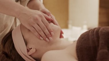 Tanımlanamayan bir kadın güzellik uzmanının masaj masasında uzanan beyaz bir kadının yüzüne nemlendirici krem sürmesi.