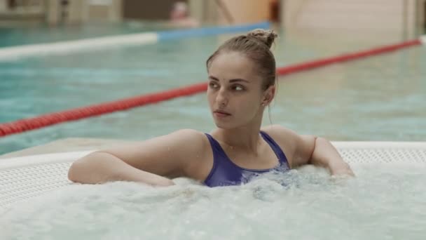 身穿蓝色游泳衣的白人年轻女子在室内温泉中心按摩浴缸放松的中照 — 图库视频影像