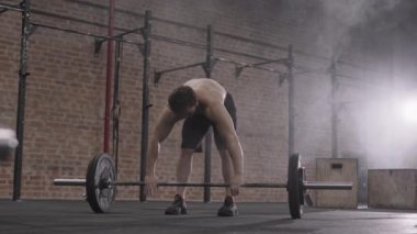 Spor kıyafetleri ve spor ayakkabıları giyen, elleri pudrayla kaplayan ve spor salonunda ağır halterleri kaldırmaya başlayan genç, kararlı beyaz tenli sporcu.